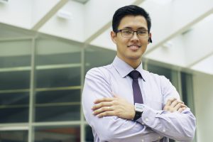 Portrait of confident asian businessman. The man stands in a street against office buildings and crosses arms looking at camera with bluetooth headset and smartwatch